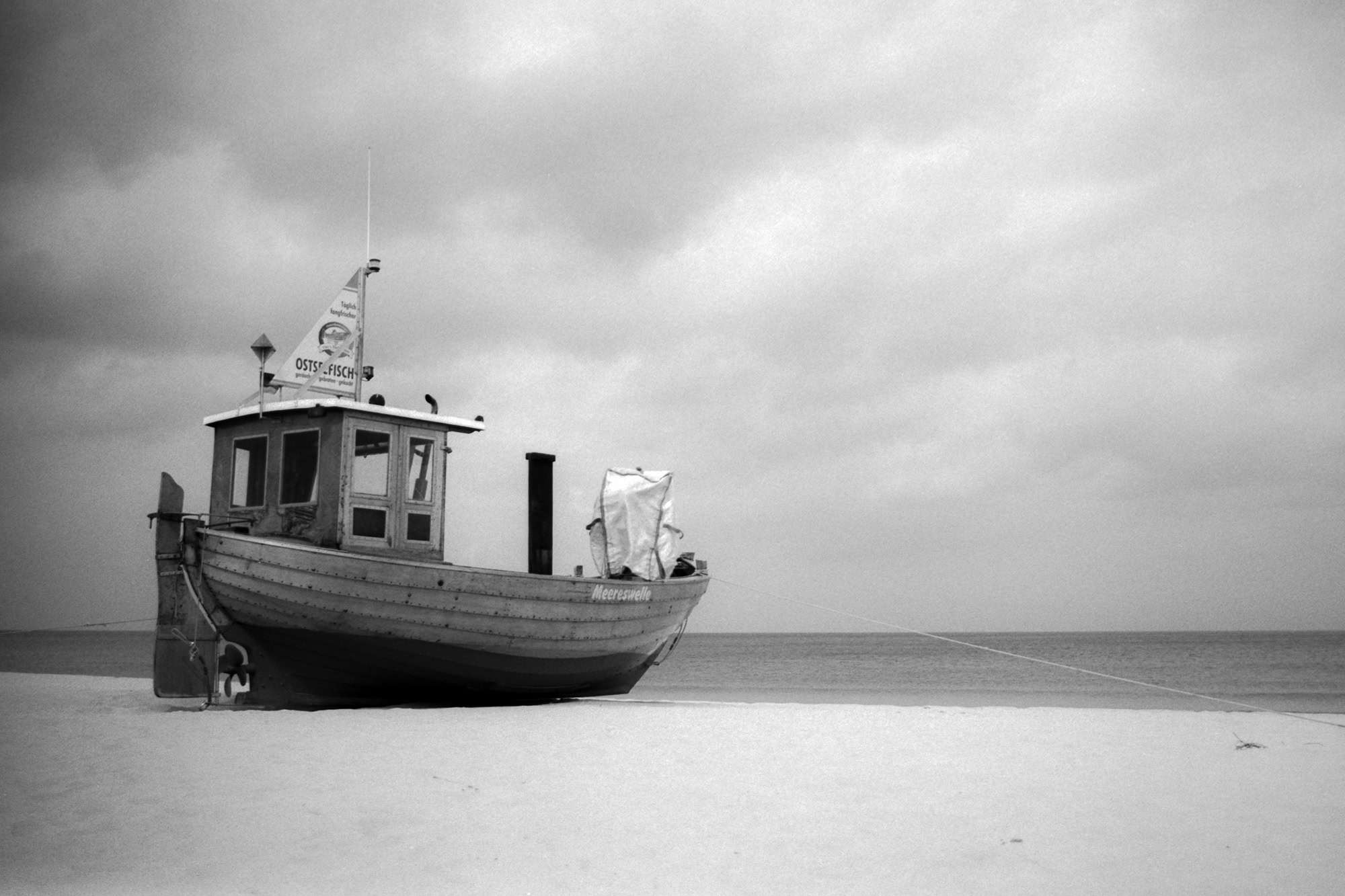 Analoges Schwarz-Weiß Foto mit einem Fischerboot namens Meereswelle am Strand, aufgenommen 2024